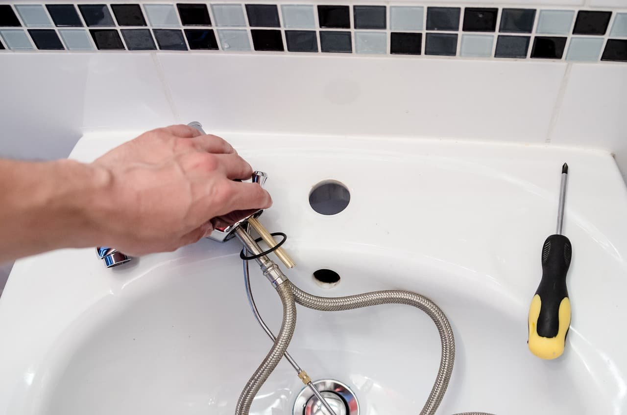 Hands fitting the flexible tails of a new tap under a white basin